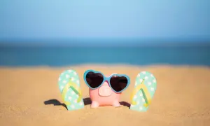 Świnka skarbonka w okularach przeciwsłonecznych i klapki na plaży. To symbol oszczędzania na wakacje ZUS.