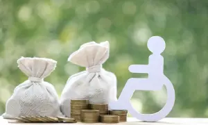Symbol osoby na wózku inwalidzkim obok worków z pieniędzmi i monet sugeruje świadczenie wspierające kwoty.
