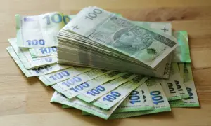 Stos banknotów 100 zł i 100 euro na drewnianym blacie. Może to być kwota na zasiłek stały.