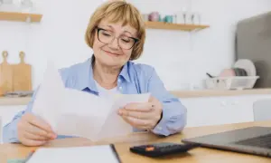 Uśmiechnięta starsza pani analizuje dokumenty, zastanawiając się, o ile wzrośnie emerytura po roku pracy na emeryturze.