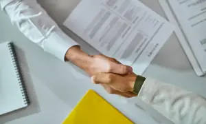 Uścisk dłoni po podpisaniu umowy stażowej. Na stole dokumenty i notatnik.