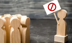 Drewniane figurki ludzi, jedna z tabliczką z przekreślonym kółkiem, symbolizującą zakaz konkurencji.