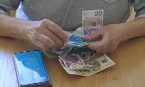 Dłonie liczą pieniądze, obok leży smartfon z kalkulatorem. Czy to dodatek pielęgnacyjny z ZUS, komu przysługuje?