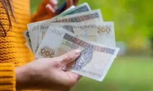 Ręka trzyma polskie banknoty 200 zł. Dowiedz się, jak obliczyć ekwiwalent za urlop, by mieć pewność, że otrzymasz należne pieniądze.
