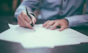 Dłoń pisze na dokumencie, zastanawiając się, ile jest ważne zaświadczenie o niekaralności.