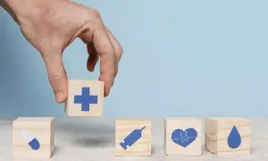 Dłoń układa kostkę z krzyżem obok kostek z pigułką, strzykawką, sercem i kroplą. To symbol tego, że podlegam obowiązkowi ubezpieczenia zdrowotnego.