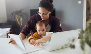 Kobieta z dzieckiem na kolanach przegląda dokumenty, być może umowa uaktywniająca dla niani.