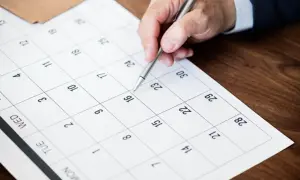 Dłoń z długopisem zaznacza datę na kalendarzu, planując urlop zgodnie z kodeksem pracy.