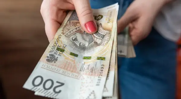 Dłoń trzyma stos banknotów 200 zł. Czekamy na przelew, kiedy ZUS robi przelewy, to zawsze radość!