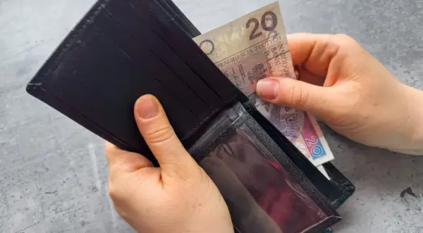 Ręce wkładają banknot 20 zł do portfela. Zastanawiasz się, po jakim czasie od zarejestrowania wypłacany jest zasiłek dla bezrobotnych?