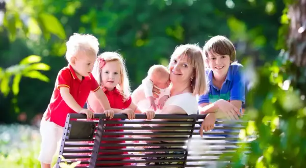 Szczęśliwa mama z czwórką dzieci na ławce w parku. Marzy o emeryturze dla matek 3 dzieci od kiedy?
