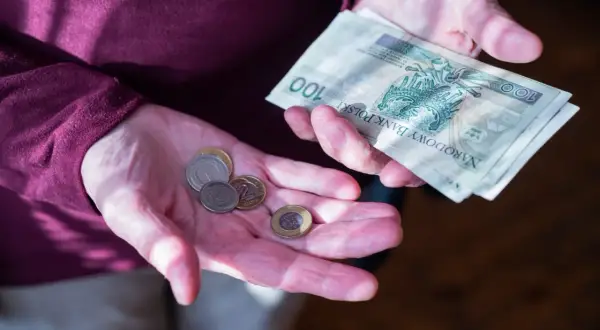 Dłonie pokazują monety i banknot 100 zł. Zastanawiasz się, ile wynosi dodatek do emerytury za warunki szkodliwe?