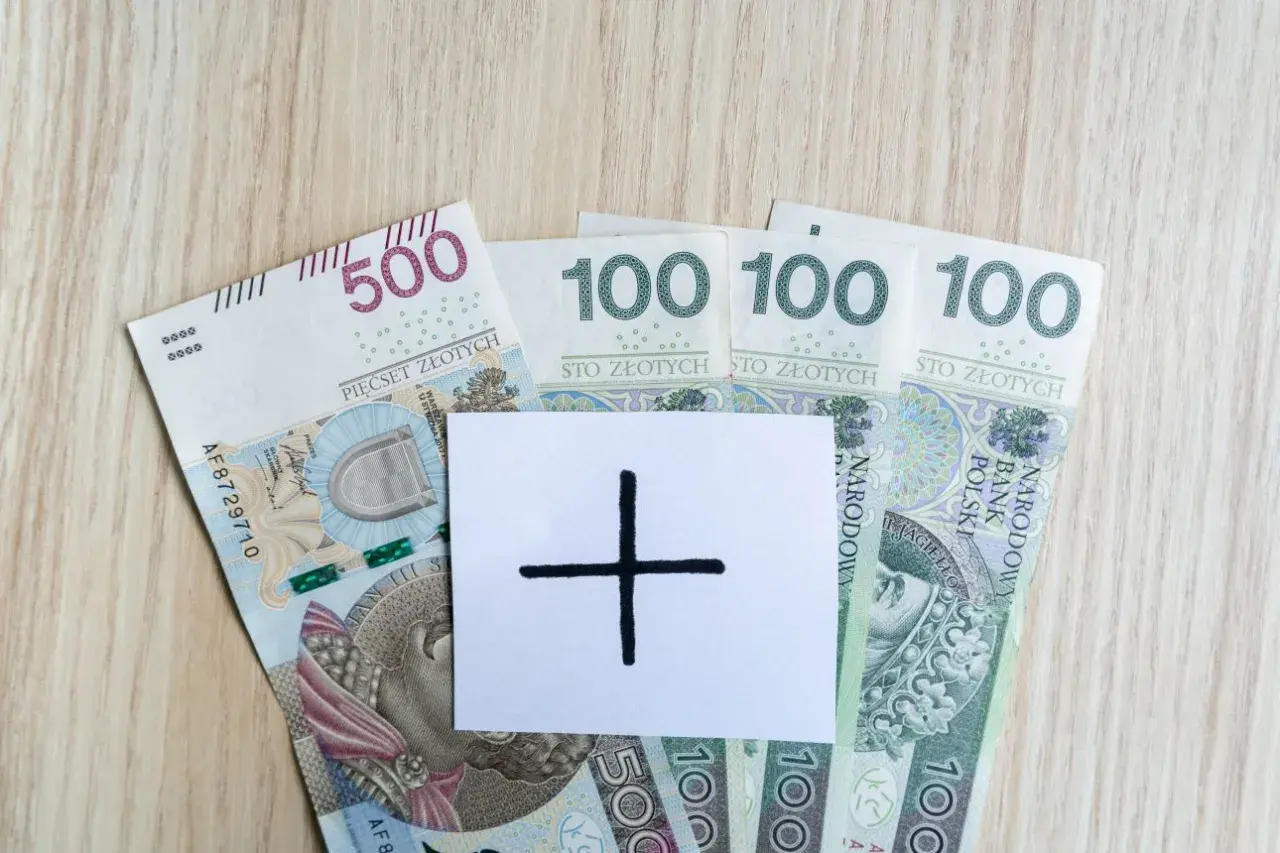 Polskie banknoty 500 i 100 zł. Na białej kartce symbol plusa, sugerujący dodatkowe środki, np. specjalny zasiłek opiekuńczy.