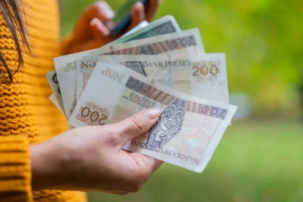 Ręka trzyma polskie banknoty 200 zł. Dowiedz się, jak obliczyć ekwiwalent za urlop, by mieć pewność, że otrzymasz należne pieniądze.