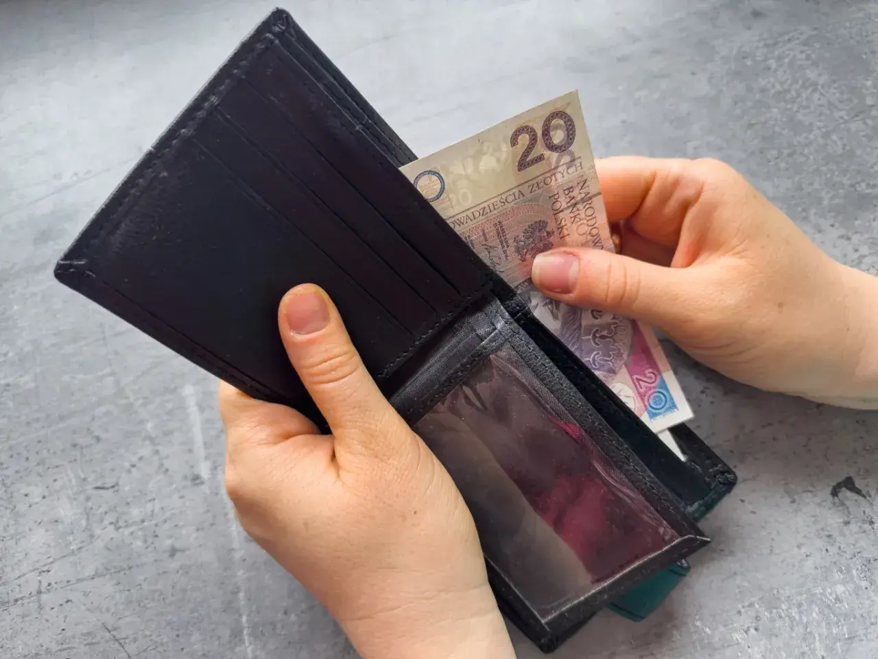 Ręce wkładają banknot 20 zł do portfela. Zastanawiasz się, po jakim czasie od zarejestrowania wypłacany jest zasiłek dla bezrobotnych?