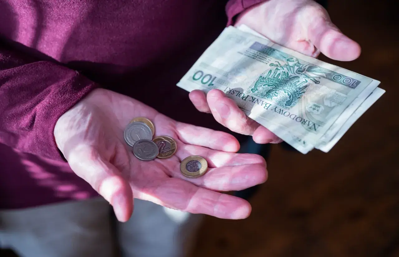 Dłonie pokazują monety i banknot 100 zł. Zastanawiasz się, ile wynosi dodatek do emerytury za warunki szkodliwe?