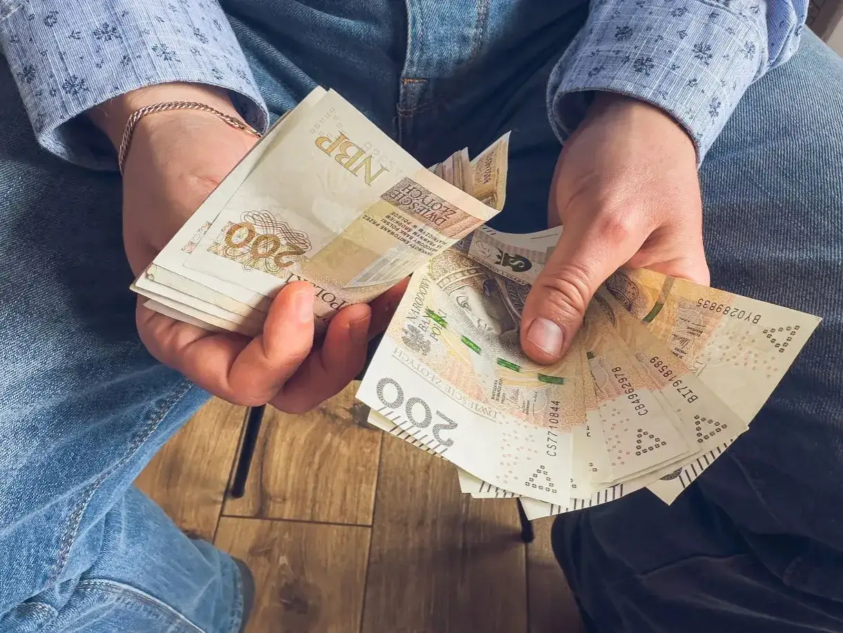 Ręce trzymające stos banknotów 200 zł. To może być wypłata, premia lub świadczenie urlopowe.