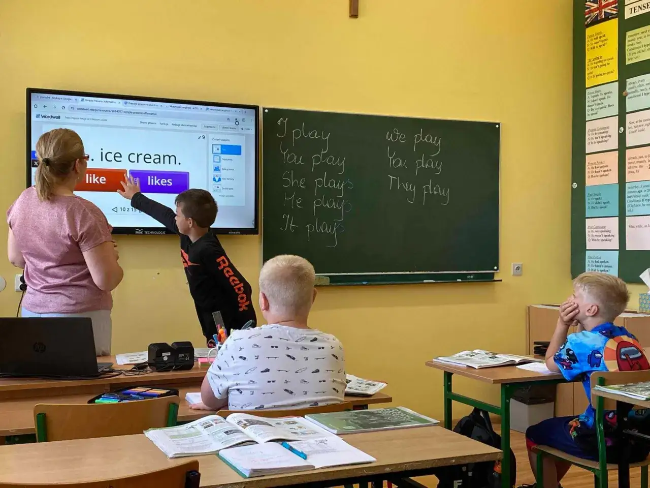Lekcja angielskiego w klasie 1-3. Nauczycielka z uczniem przy tablicy interaktywnej. Ile zarabia nauczyciel klas 1-3? To pytanie nurtuje wielu, ale dziś liczy się nauka!